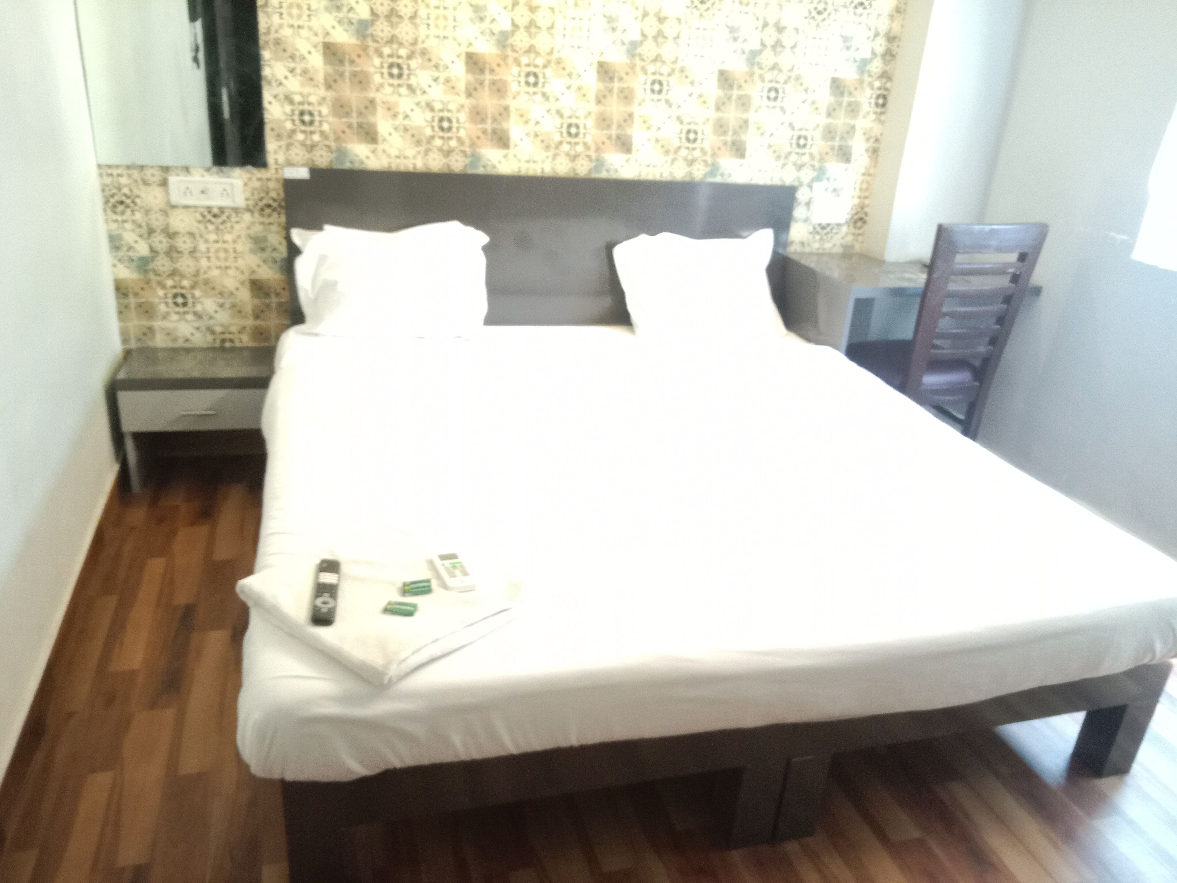 Un letto rifatto con lenzuola bianche, una testiera in legno e un comodino con una lampada.