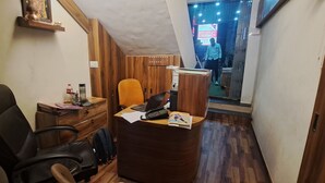 Un petit bureau avec un bureau en bois, une chaise de bureau noire, un ordinateur portable et un meuble en bois.