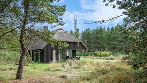 Une cabane rustique au toit de chaume, entourée d’un paysage naturel composé d’arbres et d’herbe.