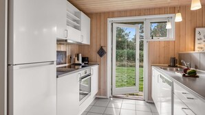 Une cuisine moderne avec des meubles blancs, une cuisinière en acier inoxydable et une grande porte-fenêtre coulissante donnant sur un jardin.