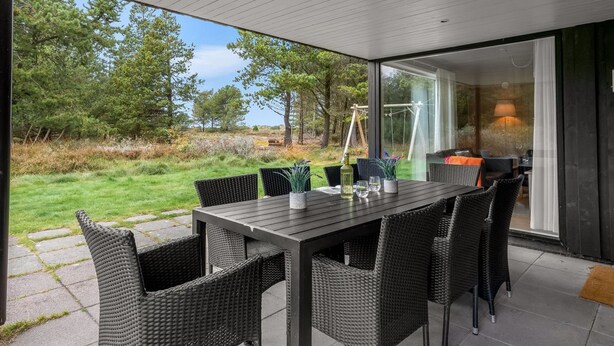 Un espace de restauration extérieur moderne, doté d'un mur de verre, de mobilier en osier et offrant une vue sur un paysage naturel.