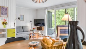 Un salon moderne avec un canapé, un téléviseur, une table à manger et une vue sur la verdure à l’extérieur.