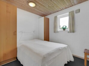 A small, single-bed room with a wooden ceiling, a window with curtains, and a small plant on the windowsill. - "Pernilla" - 2km from the sea by Interhome (Blåvand)