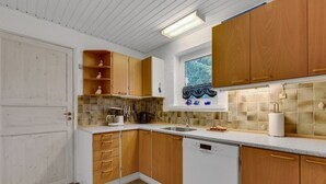 Eine Küche mit Holzausstattung, einem weißen Geschirrspüler und einem Fenster mit Blick auf Bäume.