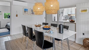 Een eethoek met een witte tafel, zwarte stoelen en rieten hanglampen.