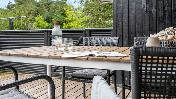 Een houten terras met een tafel, stoelen, een fles water en een mand met stenen.