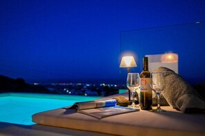 Area piscina con tavolino in vetro, una bottiglia di vino, un bicchiere, una candela e un asciugamano.