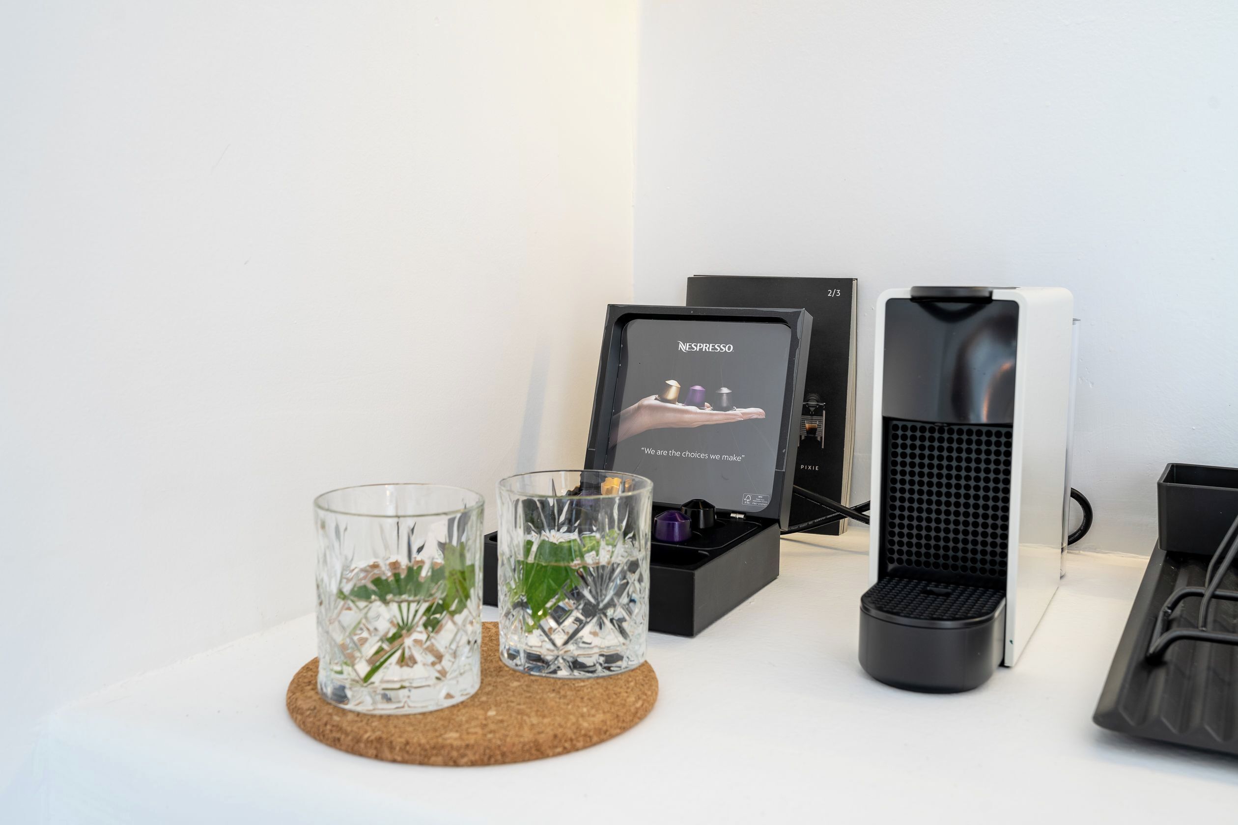 A Nespresso coffee machine, two glass cups with plants, and a black box with a Nespresso logo.