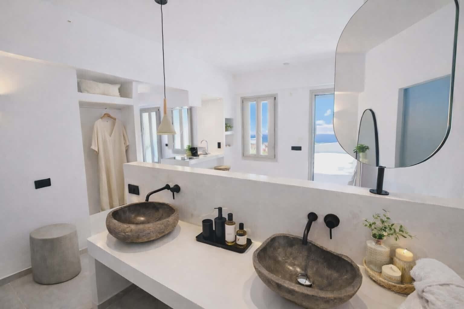 A modern bathroom with two large stone sinks, a mirror, and a view of the sea.