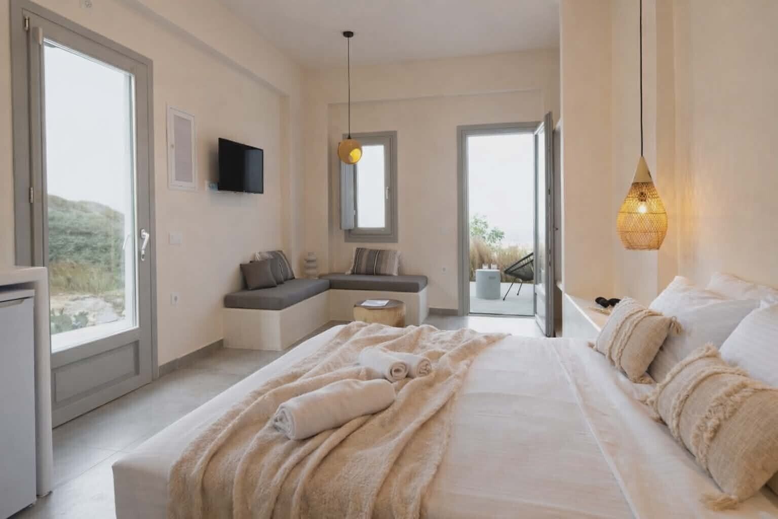 Ein Schlafzimmer mit einem großen Bett, einer Sitzecke, einem Fernseher und einem Balkon.