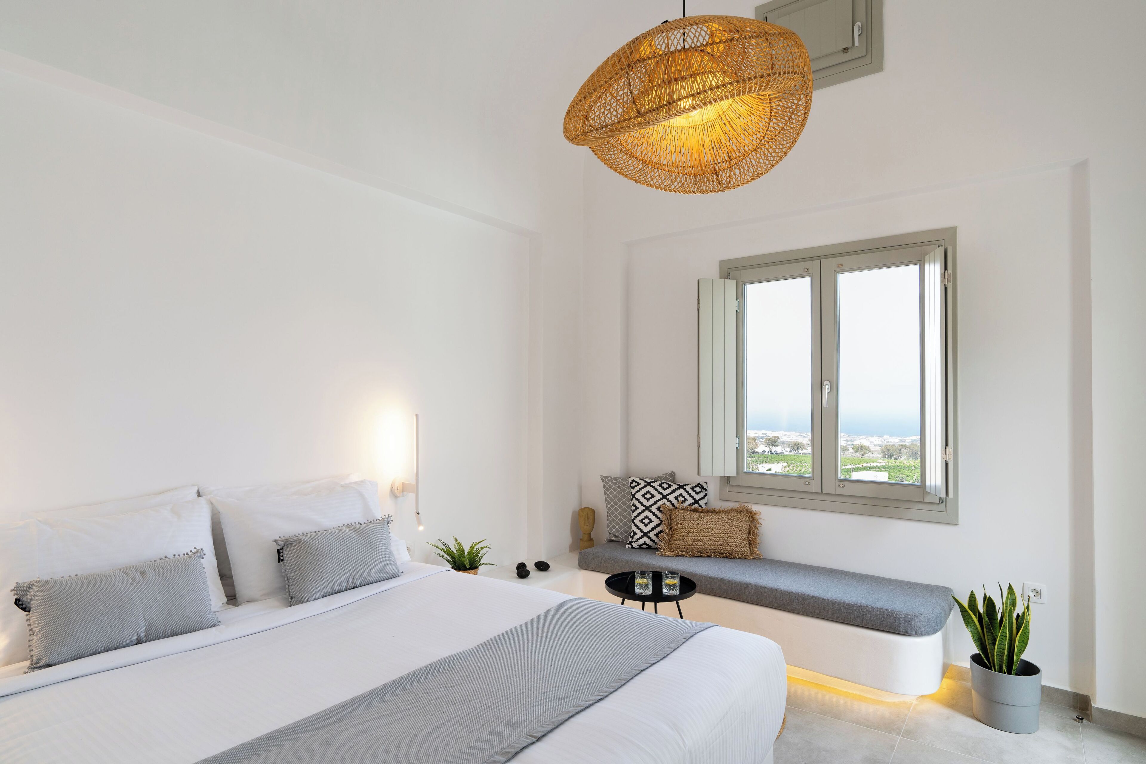 A modern bedroom with a large bed, a bench by the window, and a view of the outdoors.