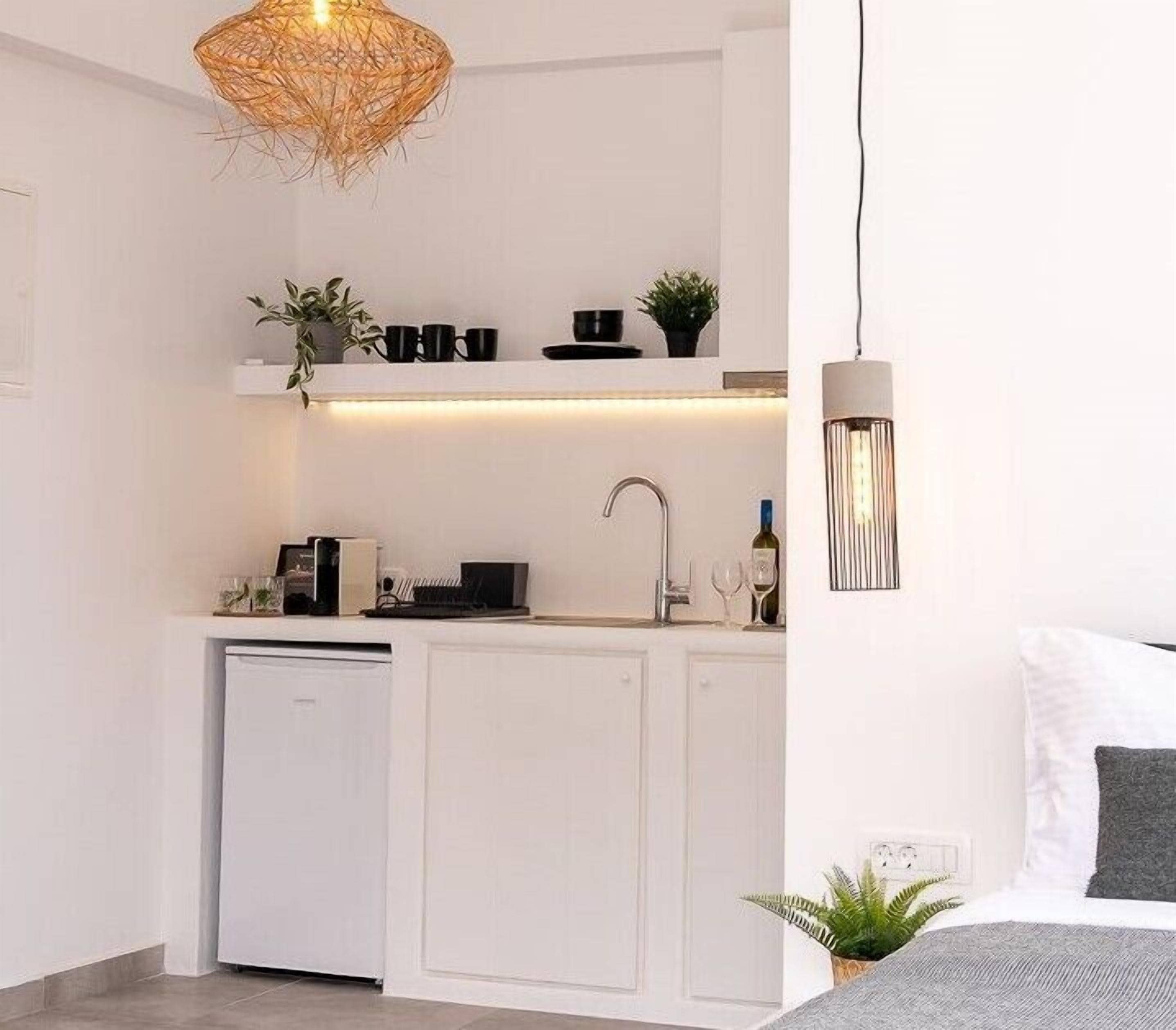A compact kitchen with white cabinetry, a built-in dishwasher, and a hanging light fixture.