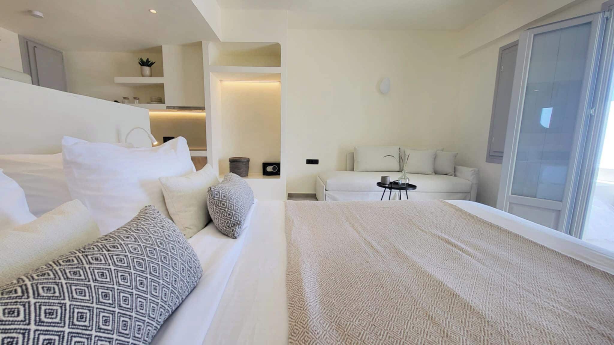 A modern hotel room with a large bed, a sofa, a small table, and a balcony with a sliding door.