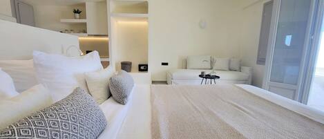 A modern hotel room with a large bed, a sofa, a small table, and a balcony with a sliding door.