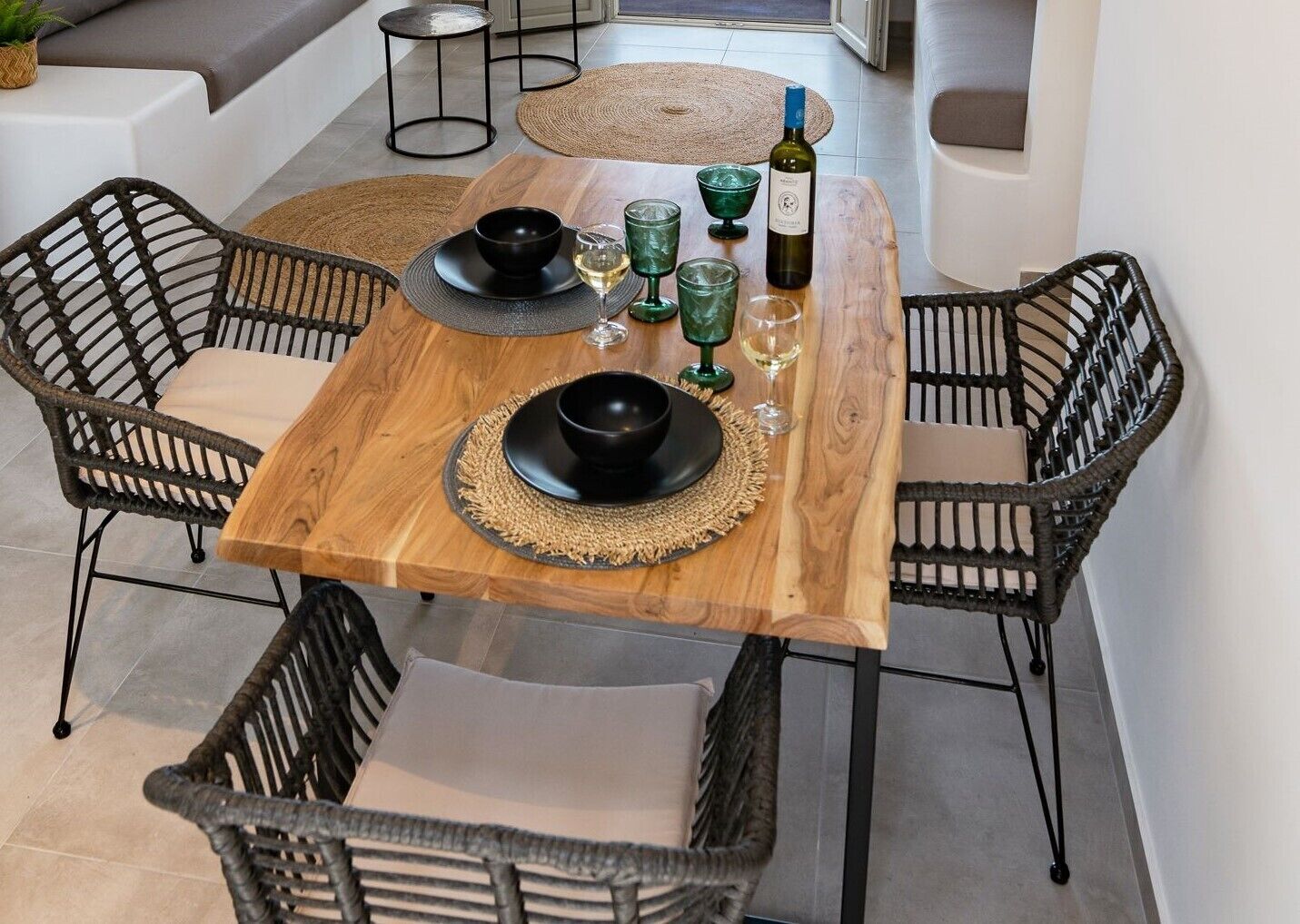 A dining area with a wooden table, black bowls, green glasses, and a bottle of wine.