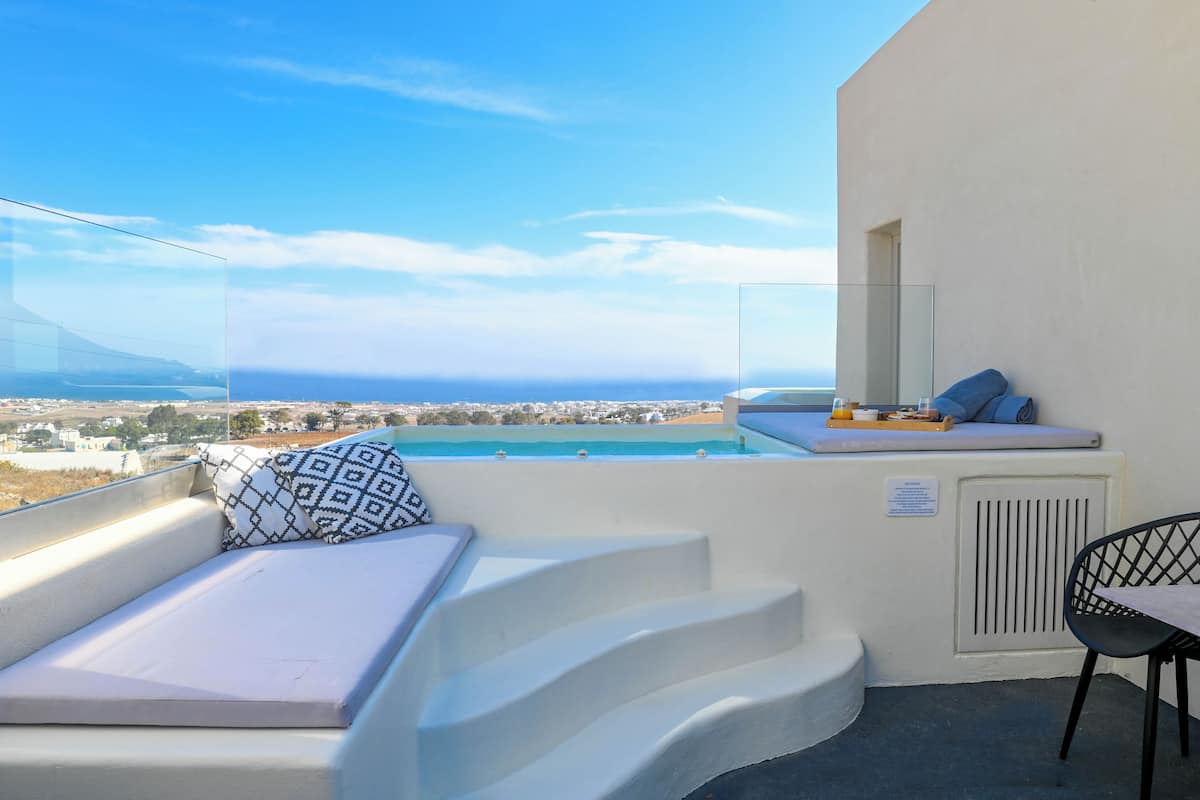 A balcony with a view of the sea, white furniture, and a small table with a glass.