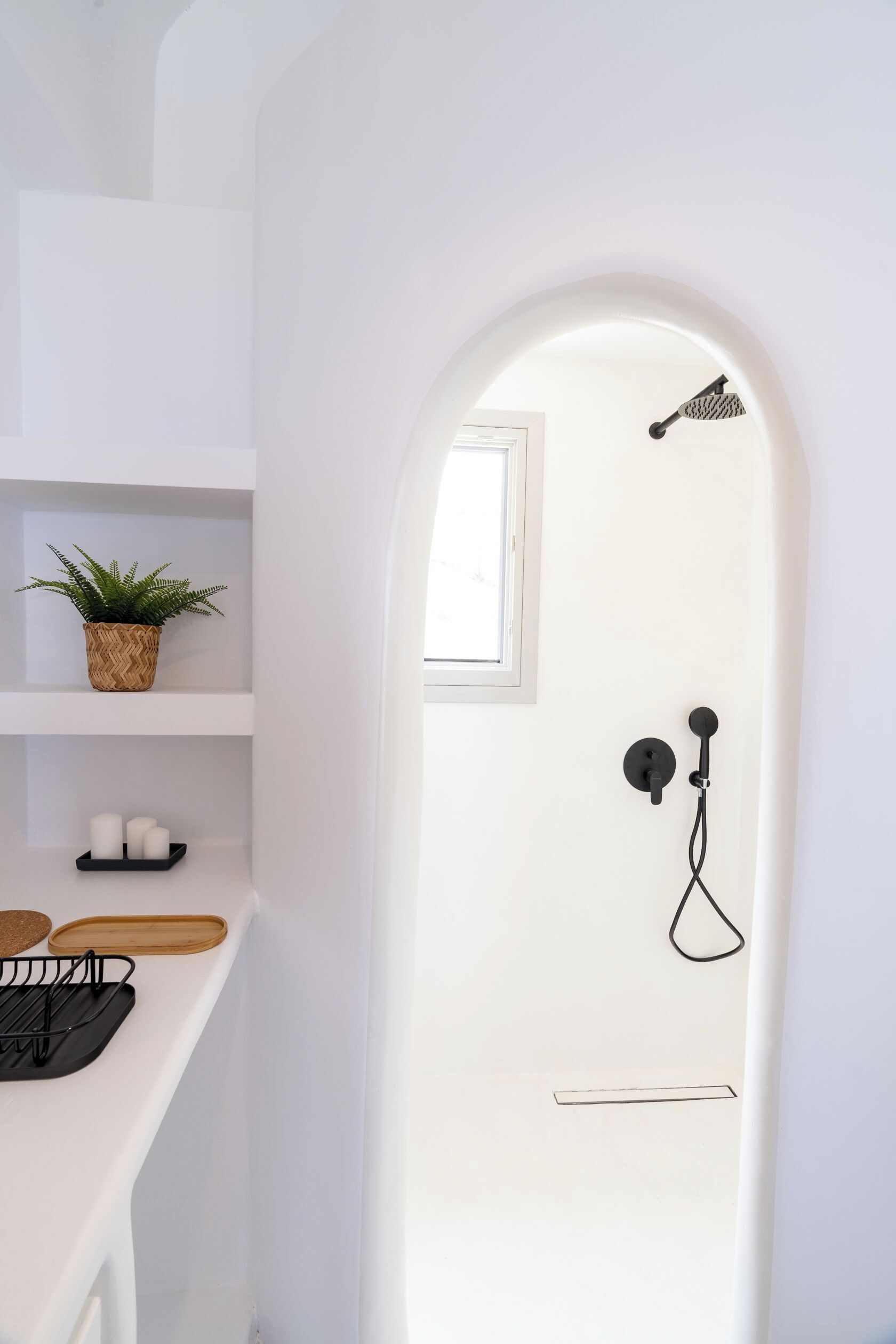 A minimalist bathroom with a shower, a small window, and a shelf with a plant and candles.