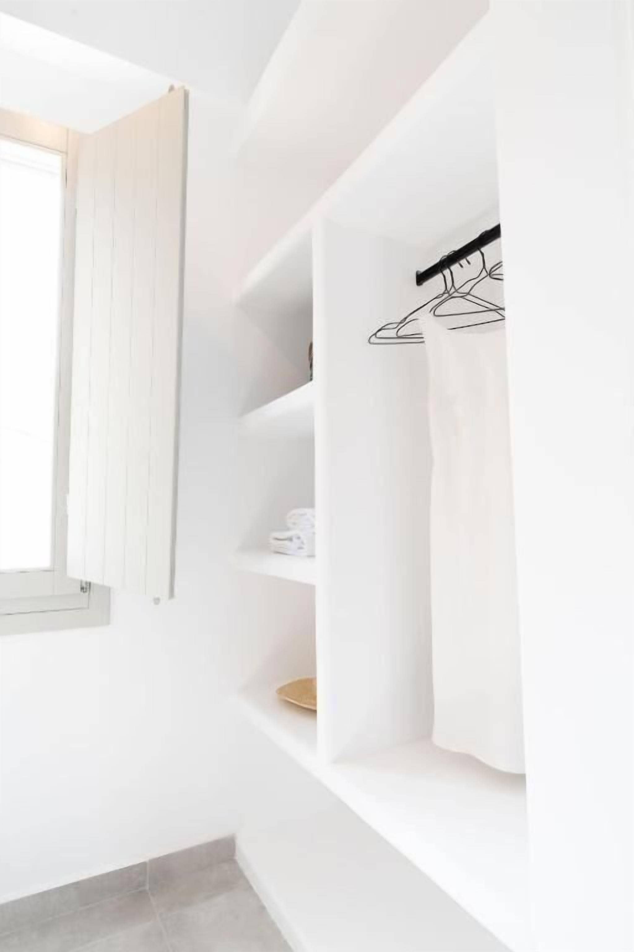 Un interior blanco con ventana, estantes blancos y un perchero colgado.