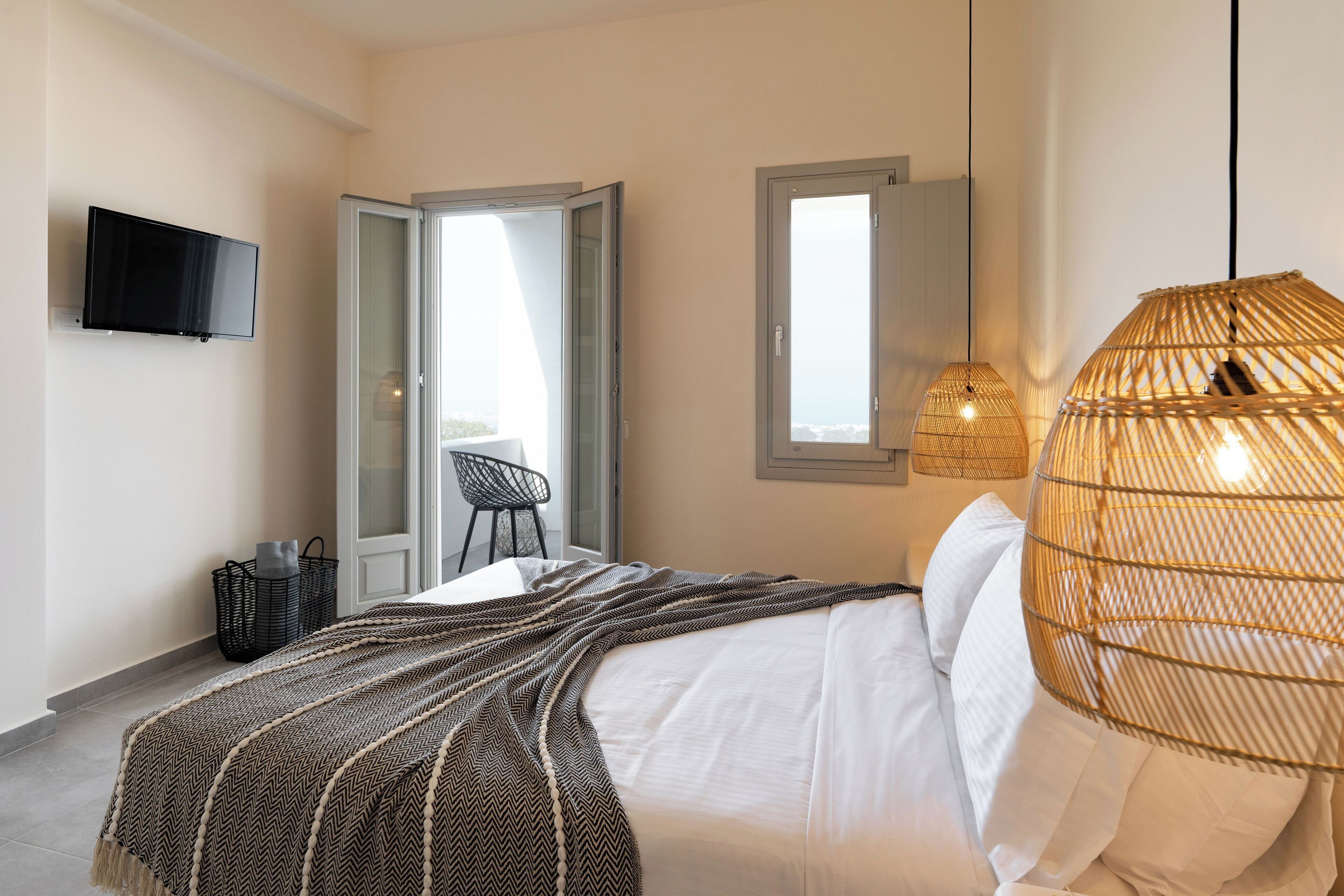 A bedroom with a bed, a television, a window, and a wicker lamp.