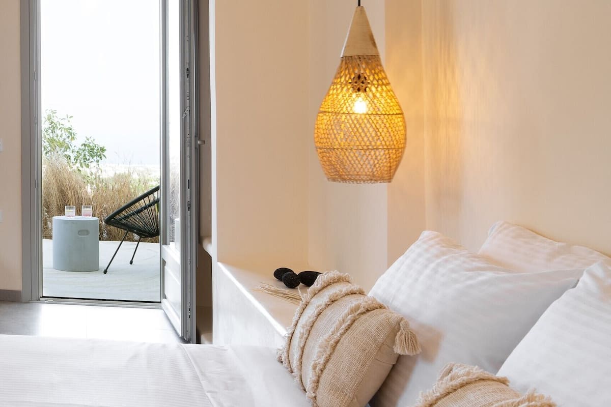 A bedroom with a bed, a hanging light fixture, and a view of an outdoor area with a chair and table.