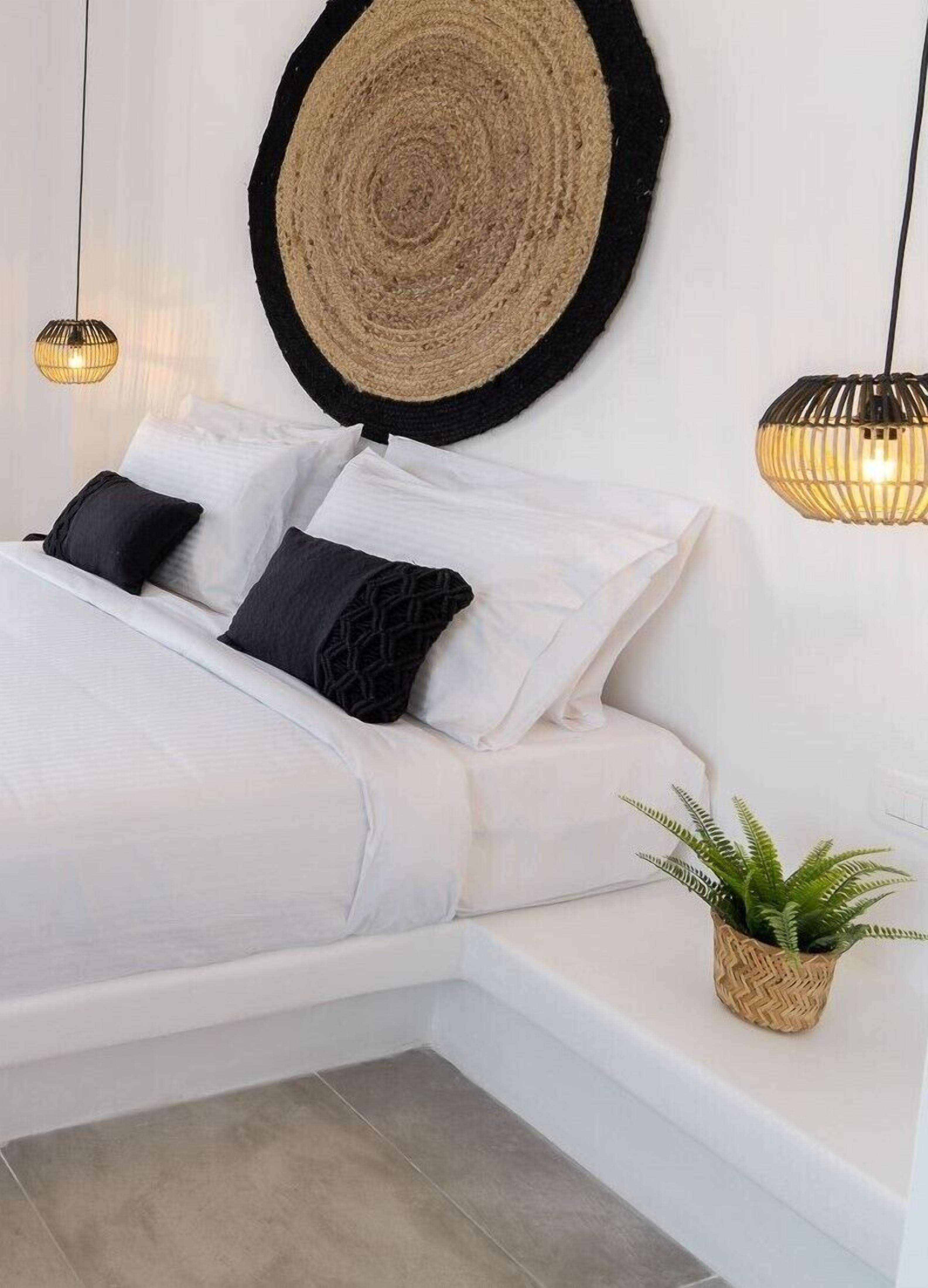 Un dormitorio con cama, almohadas, un tapiz de pared tejido, dos lámparas colgantes y una planta en maceta.