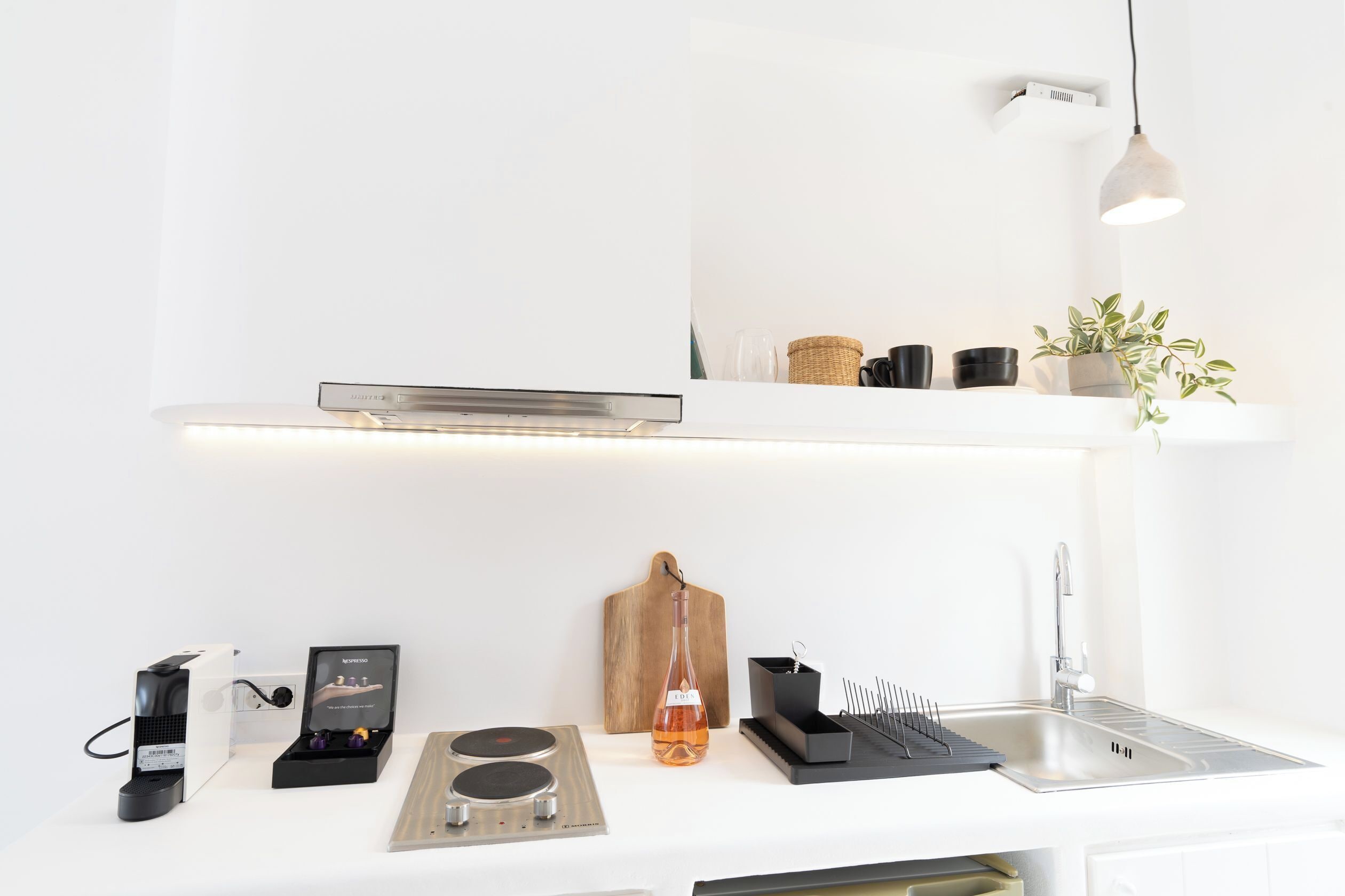 A modern kitchen with a built-in stove, a coffee machine, a hanging light, and a wooden cutting board.