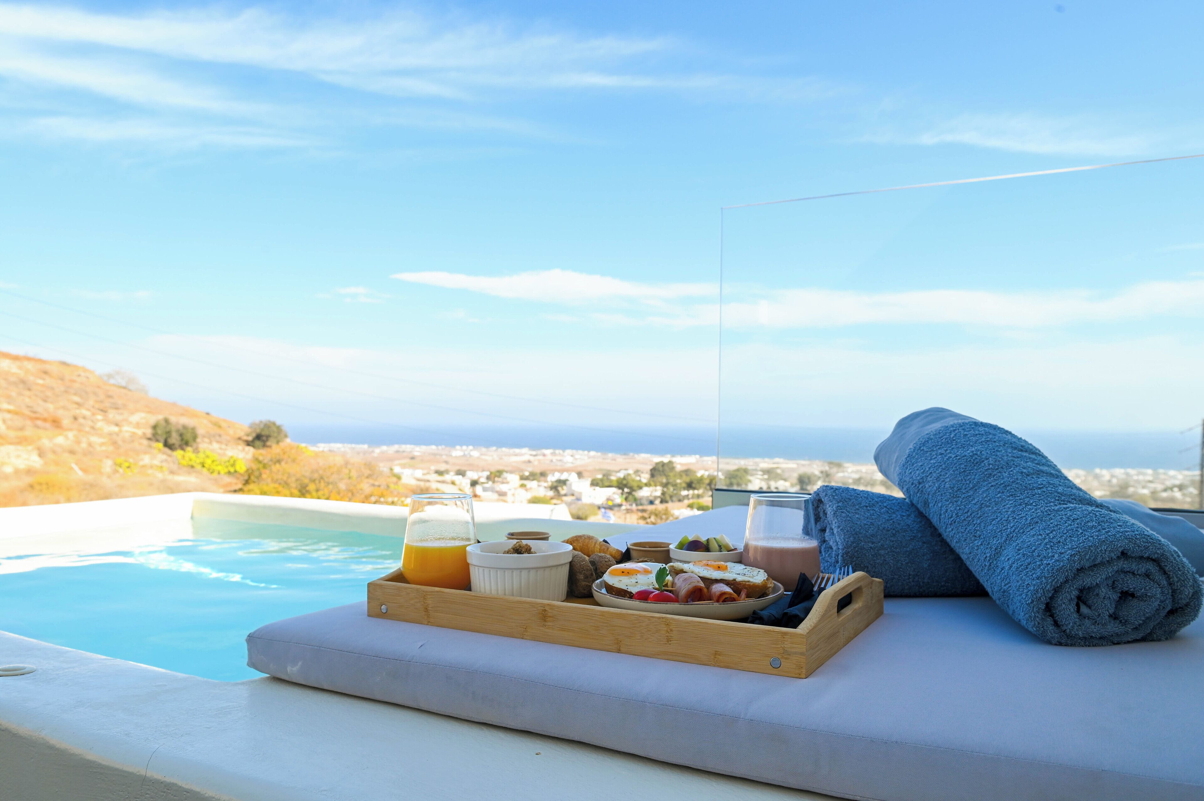 A breakfast tray with food and drinks by a pool with a view of the landscape.