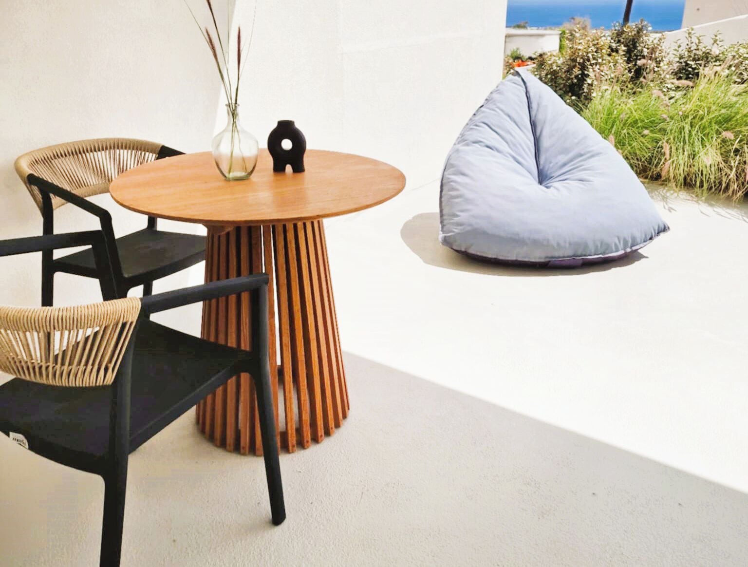A round wooden table with a vase and a black object on it, surrounded by wicker chairs.