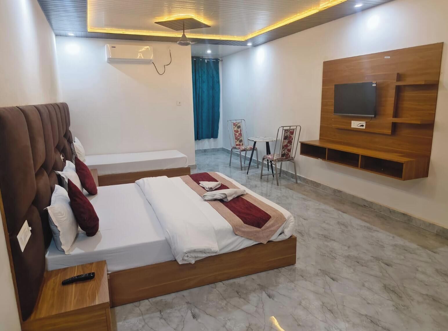 A hotel room with a bed, a TV mounted on the wall, a seating area with chairs, and a small table.