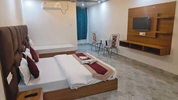 A hotel room with a bed, a TV mounted on the wall, a seating area with chairs, and a small table.