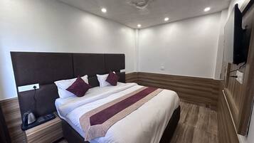 Moderni hotellihuone, jossa on suuri sänky, yöpöytä, seinälle asennettu televisio ja yksi seinä on koristeltu puupaneloinnilla.