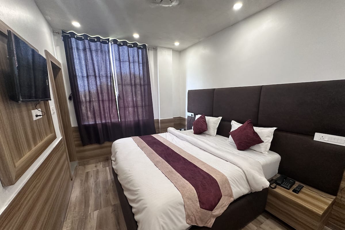 Quarto de hotel moderno com uma cama grande, piso de madeira, televisão de tela plana na parede e mesa de cabeceira com telefone e controle remoto.