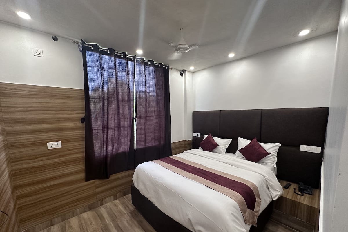 Quarto com cama, cortinas, ventoinha no teto e mesa de cabeceira com telefone.