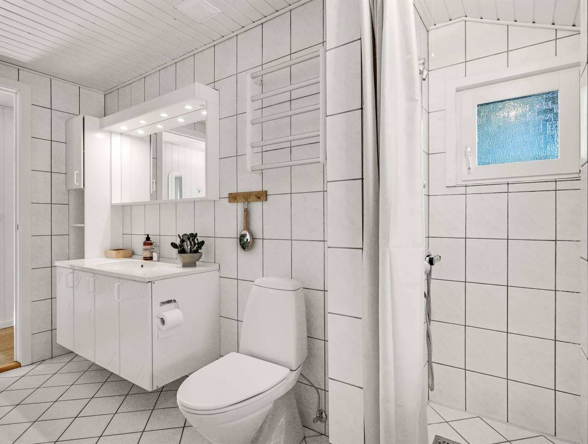 Une salle de bain moderne avec des toilettes blanches, un lavabo surmonté d’un miroir et un espace douche doté d’une fenêtre.
