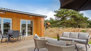 A wooden deck with outdoor furniture, a glass door entrance, and a play structure in the background. - "Dirtje" - 200m from the sea by Interhome (Blåvand)