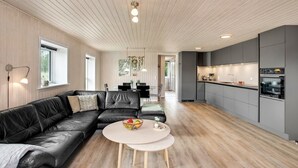 A modern living room with a black leather sofa, a round coffee table, and a dining area with a white table and chairs. - "Dirtje" - 200m from the sea by Interhome (Blåvand)