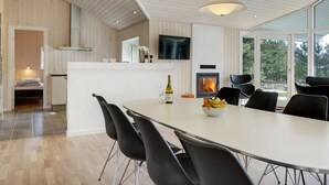 Une cuisine moderne dotée d’un îlot central, d’un coin repas avec des chaises noires, d’une cheminée et d’un téléviseur fixé au mur.