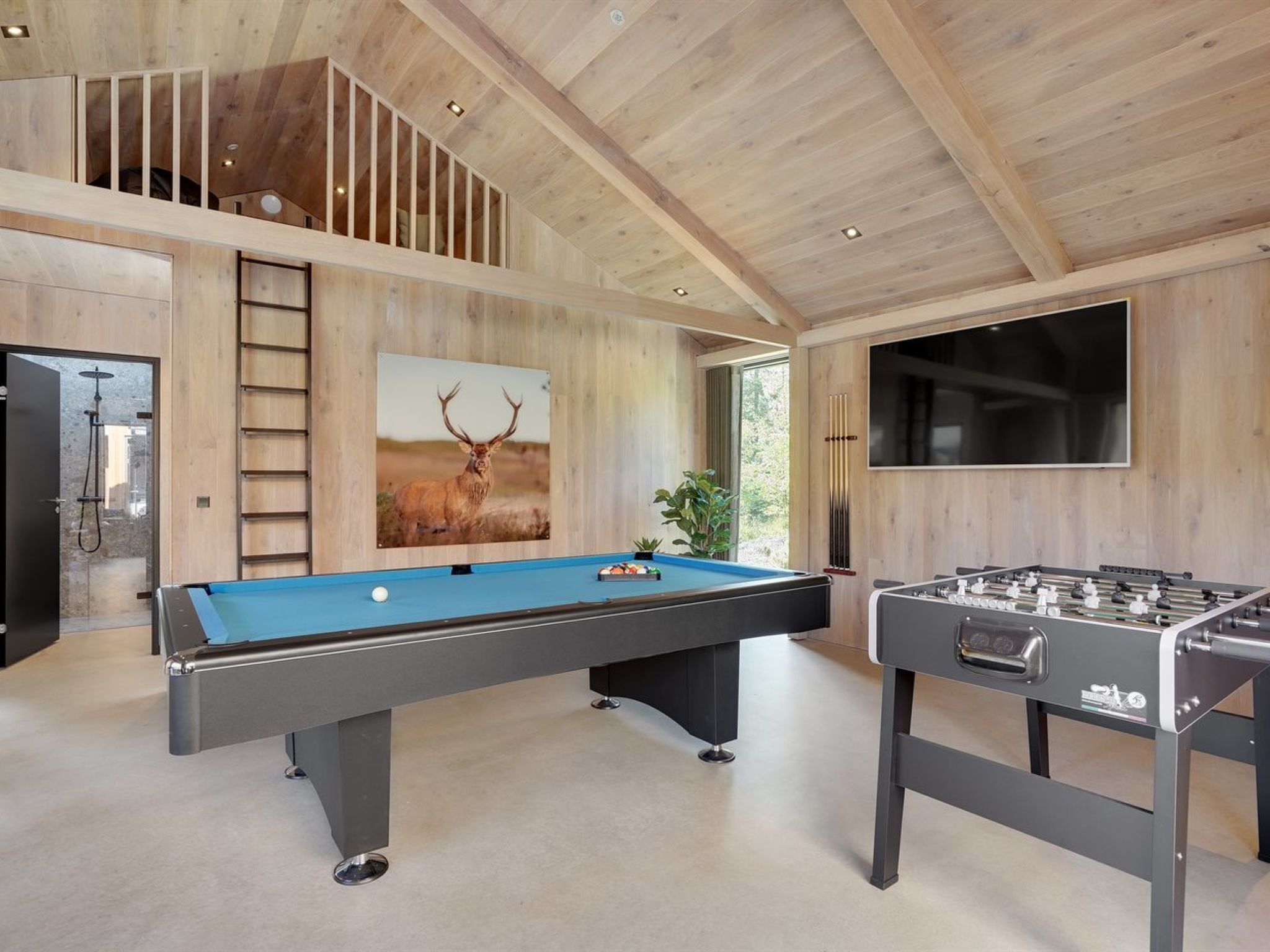 A modern indoor recreational area with a pool table, foosball table, and a large TV screen.