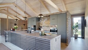 Een moderne keuken met een groot eiland, inbouwapparatuur en een accentmuur van steen.