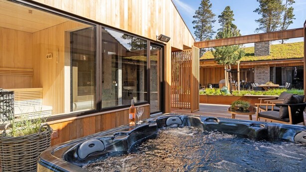 Een modern buitengebied met een hottub, houten terrassen, een spa-ruimte met glazen wanden en een terras met tuinmeubilair.