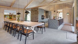 Een ruime keuken met een groot eiland, houten balken in het plafond en moderne hanglampen.