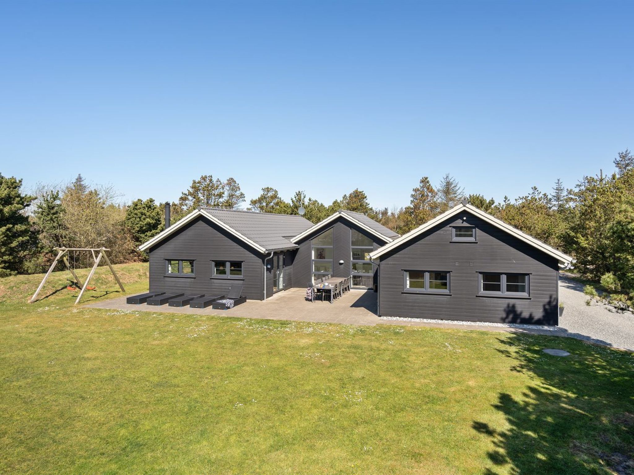A modern two-story house with a patio area, a swing set, and a well-maintained lawn.