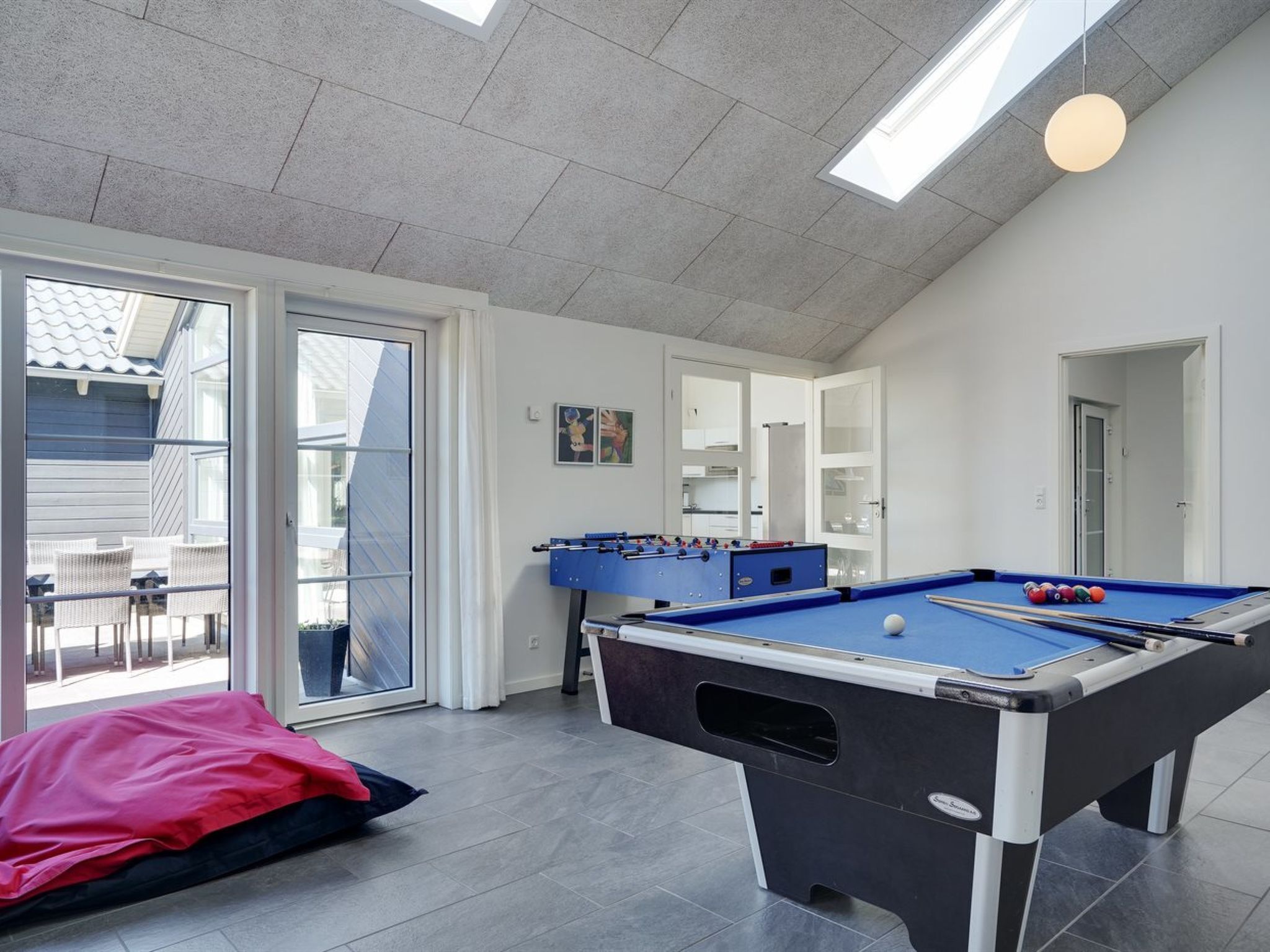 A pool table in a room with a view through a glass door, a foosball table, and a red bean bag chair.