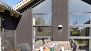 Un espace de restauration en plein air avec une table et des chaises en bois, de grandes fenêtres et une façade de bâtiment moderne.