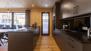 A modern kitchen with wooden cabinetry and a central island, a dining area with a table and chairs, and a view of the outside through large windows.