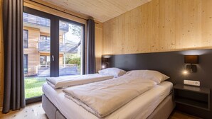 A bedroom with two beds, a wooden ceiling, a large window with curtains, and a nightstand with a lamp.