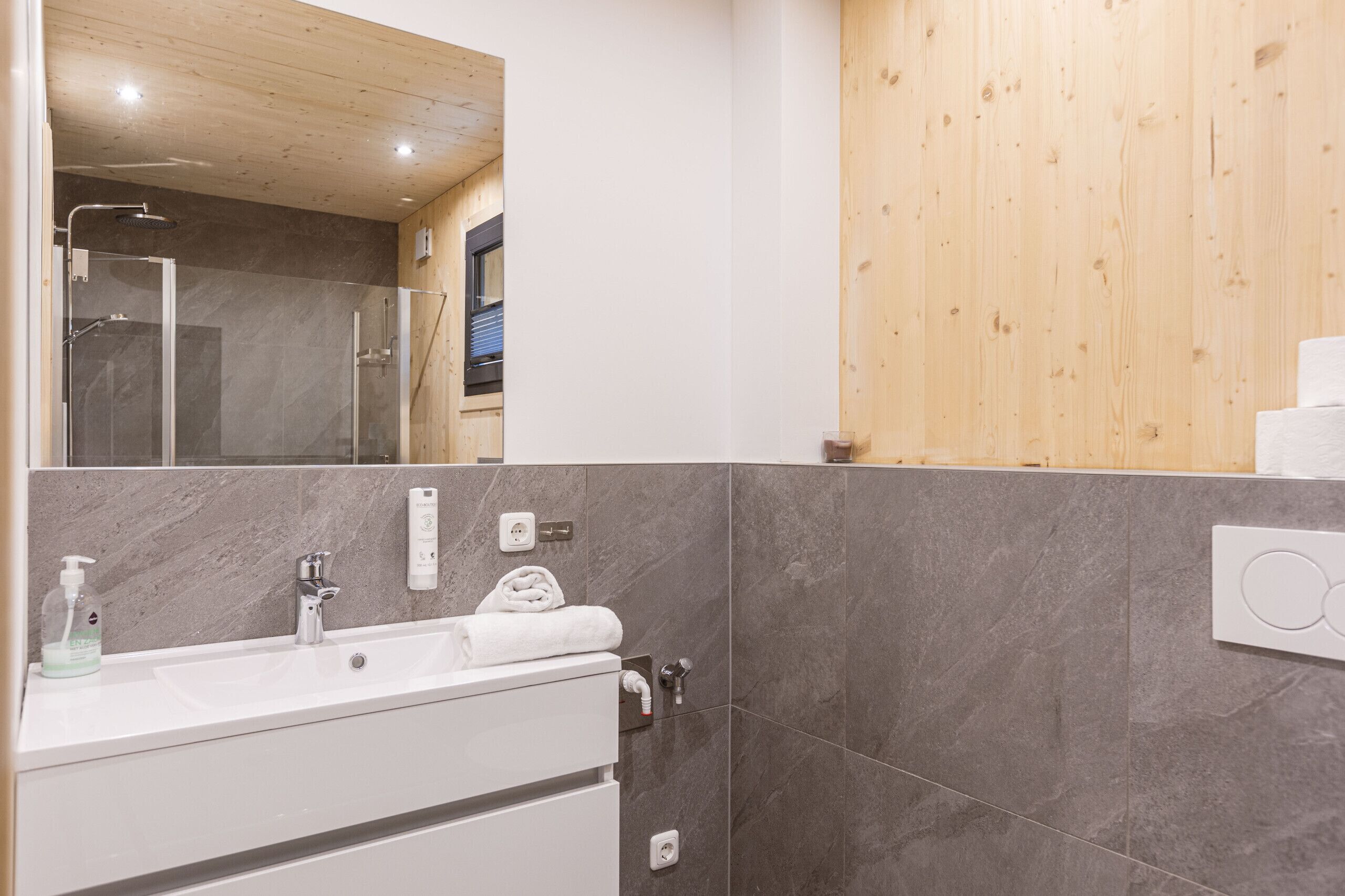 A modern bathroom with a white sink, marble tiles, and wooden paneling.