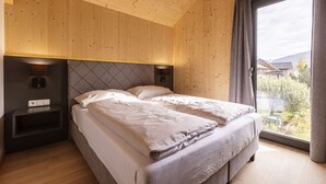 Quarto com duas camas, teto de madeira e uma janela grande com cortinas.