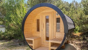Eine runde Holzsauna mit zwei Bänken und einer Tür, eingebettet in eine natürliche Umgebung.