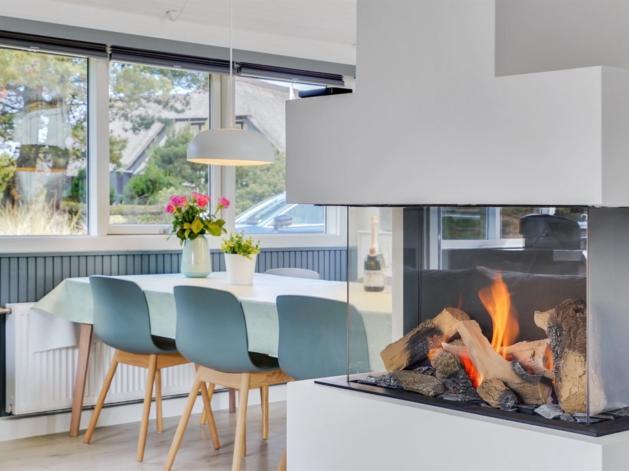 A modern dining area with a fireplace, a table with chairs, and a view of the outdoors.